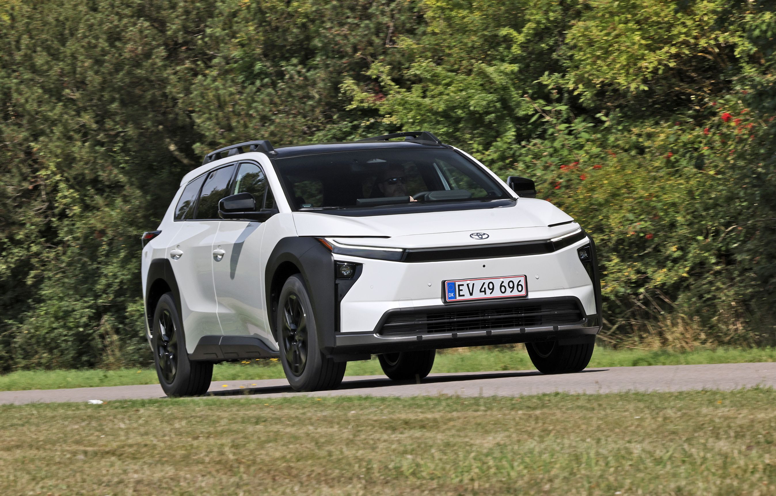 Toyota bZ4X Touring AWD Executive 2026 set forfra på landevej med grønne buske i baggrunden og græs i forgrunden.