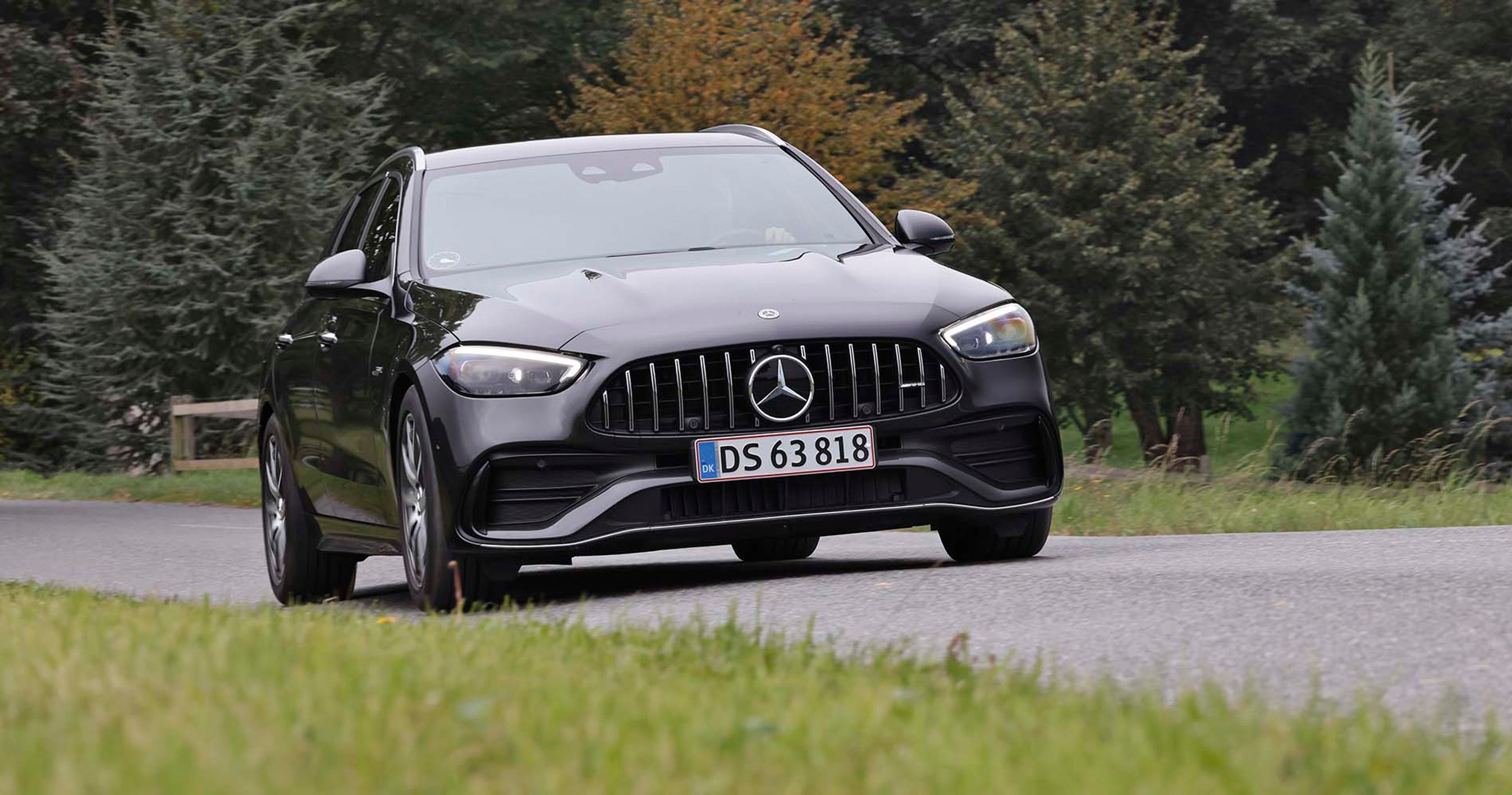 En sort Mercedes C 43 AMG kører i et sving på en landevej med træer i baggrunden.