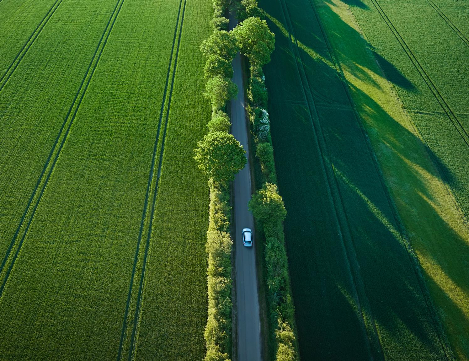 Bil set oppefra kører på landevej i sommersol