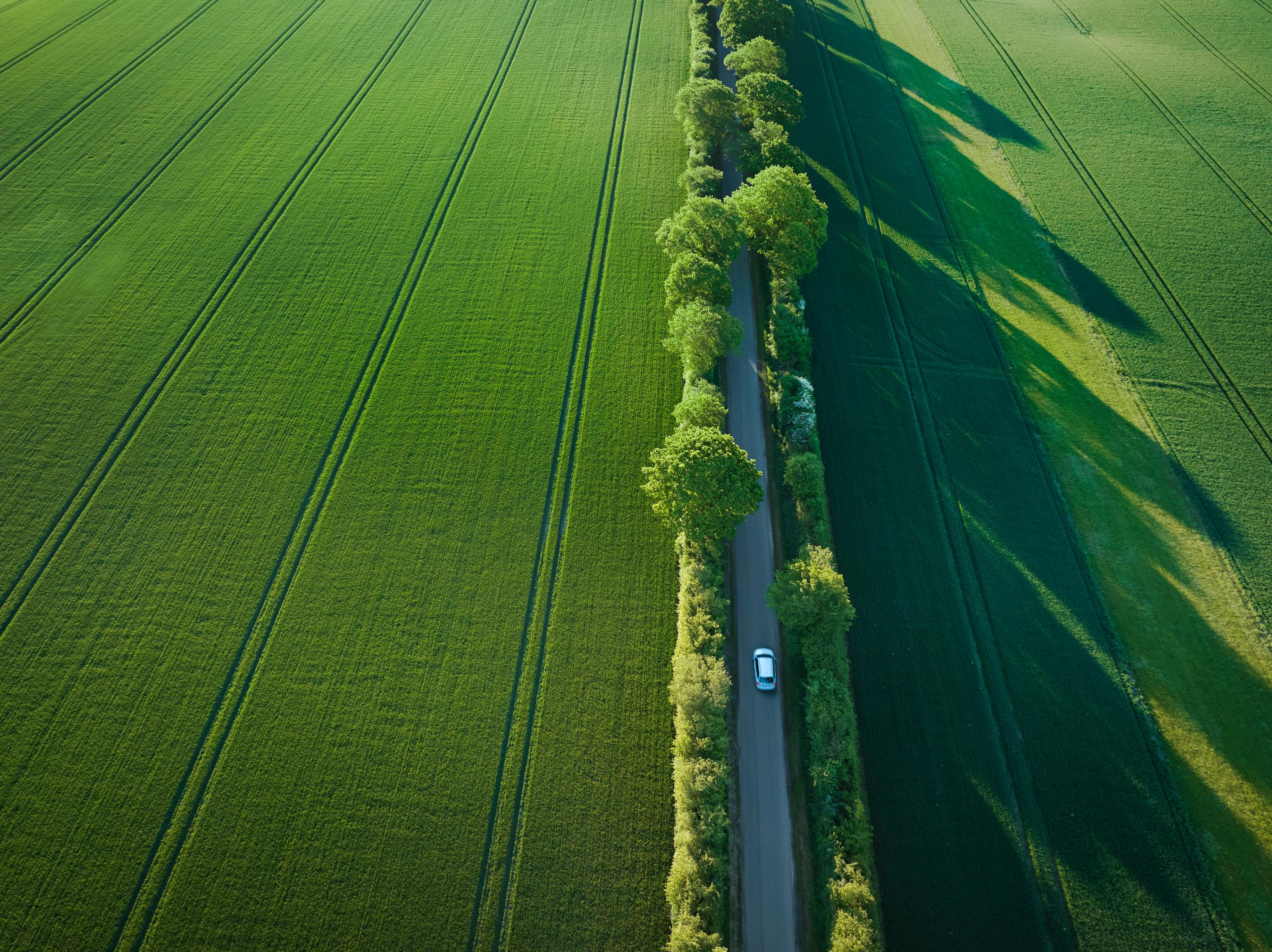 Bil set oppefra kører på landevej i sommersol