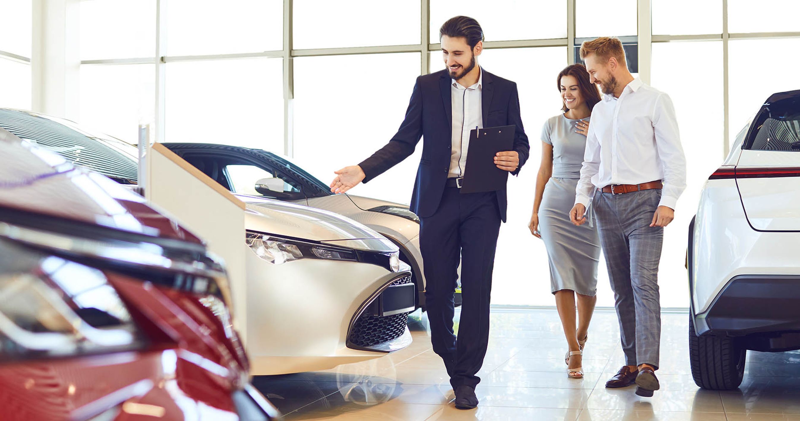 Et par ser på bil hos en forhandler. Forhandler viser nye biler frem. 