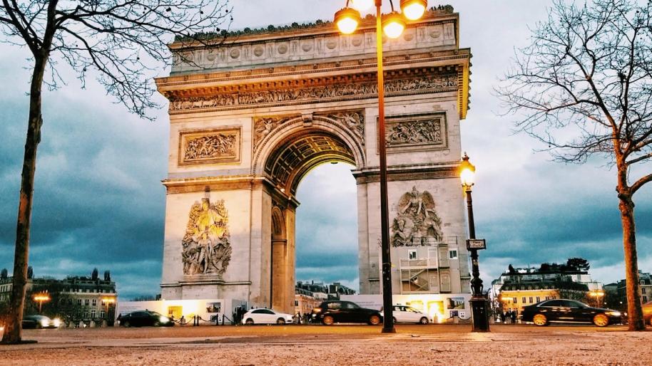 The Arc de Triomphe at winter dusk, streetlights on, trees bare of leaves.