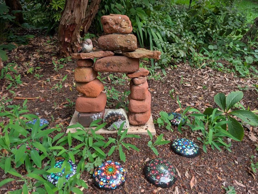 My garden: a stacked stone inukshuk with a small bird perched on it, and my painted stones set into the beds around it