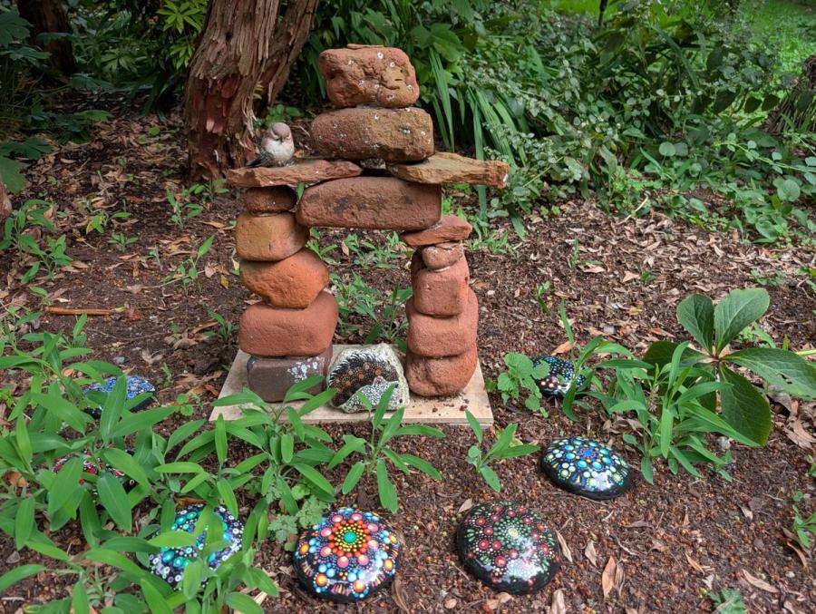 My garden: a stacked stone inukshuk with a small bird perched on it, and my painted stones set into the beds around it