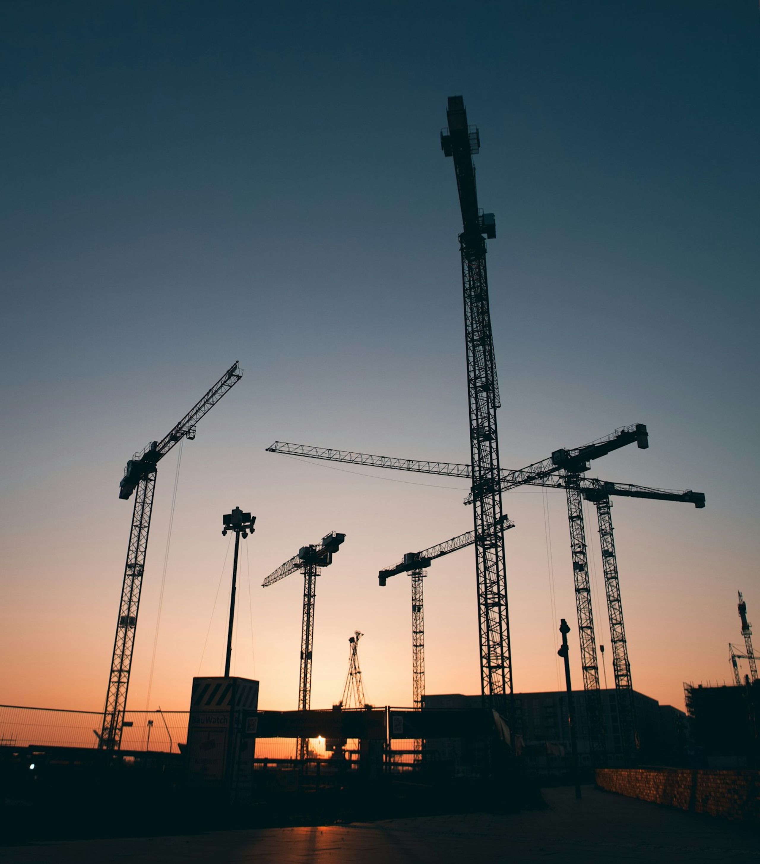 Tower cranes silhouetted against a sunset sky
