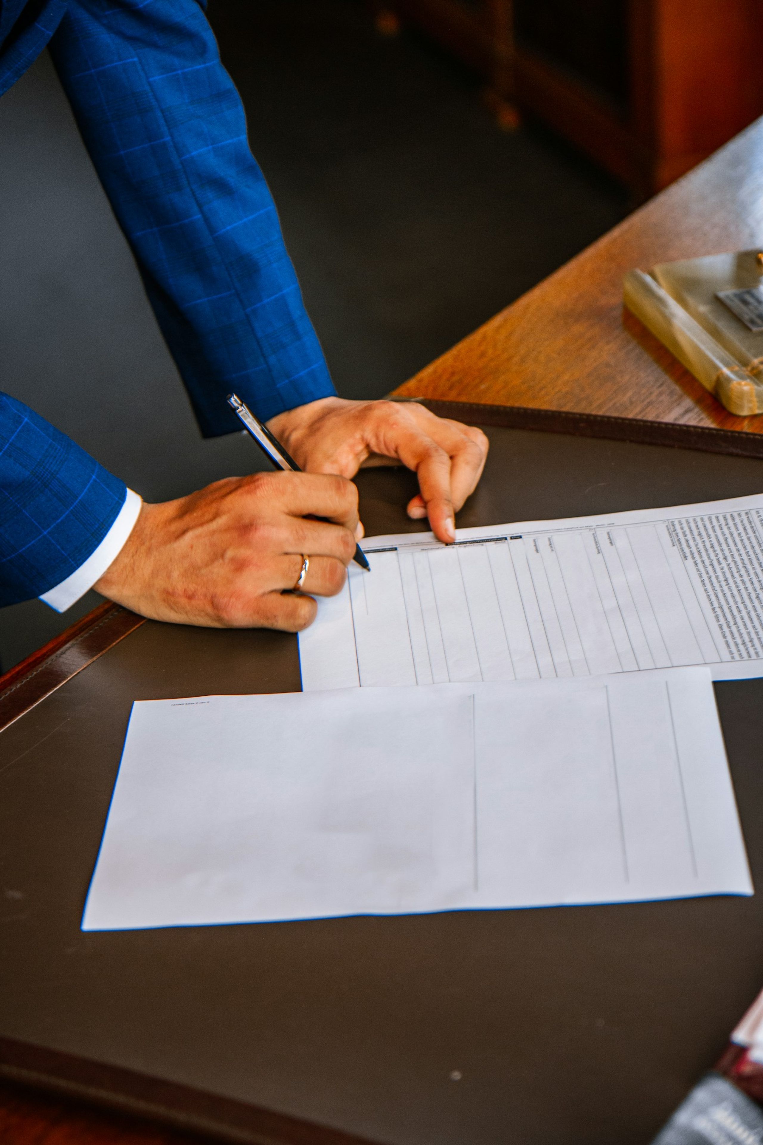 Person in a suit signing a document at a leather-topped desk