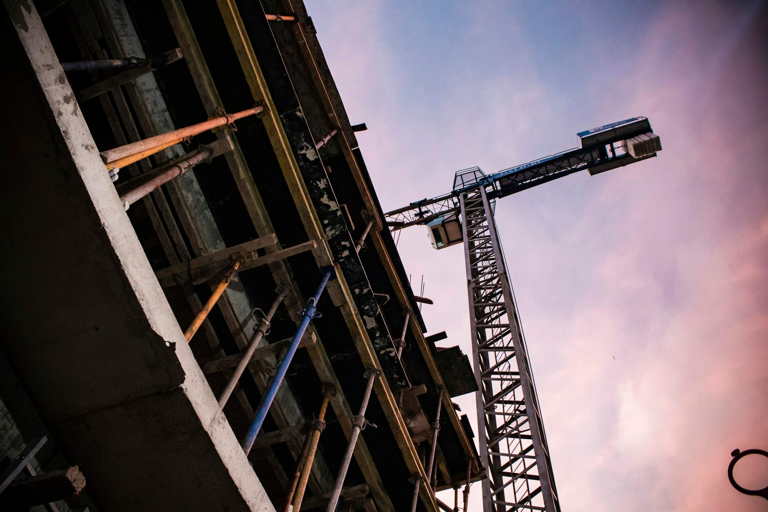 Tower crane rising beside a concrete building under construction at dusk