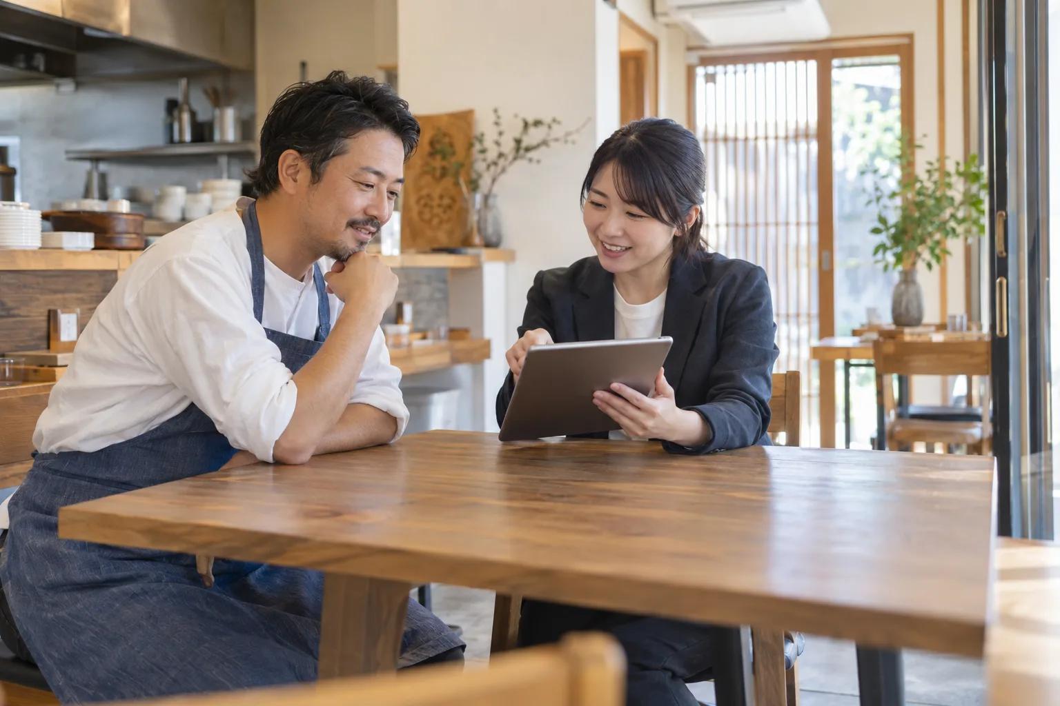 店主と相談担当者がタブレットを一緒に確認する場面（生成イメージ）