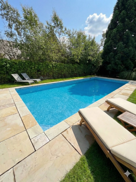 Rectangular swimming pool with paving and sun loungers in a back garden