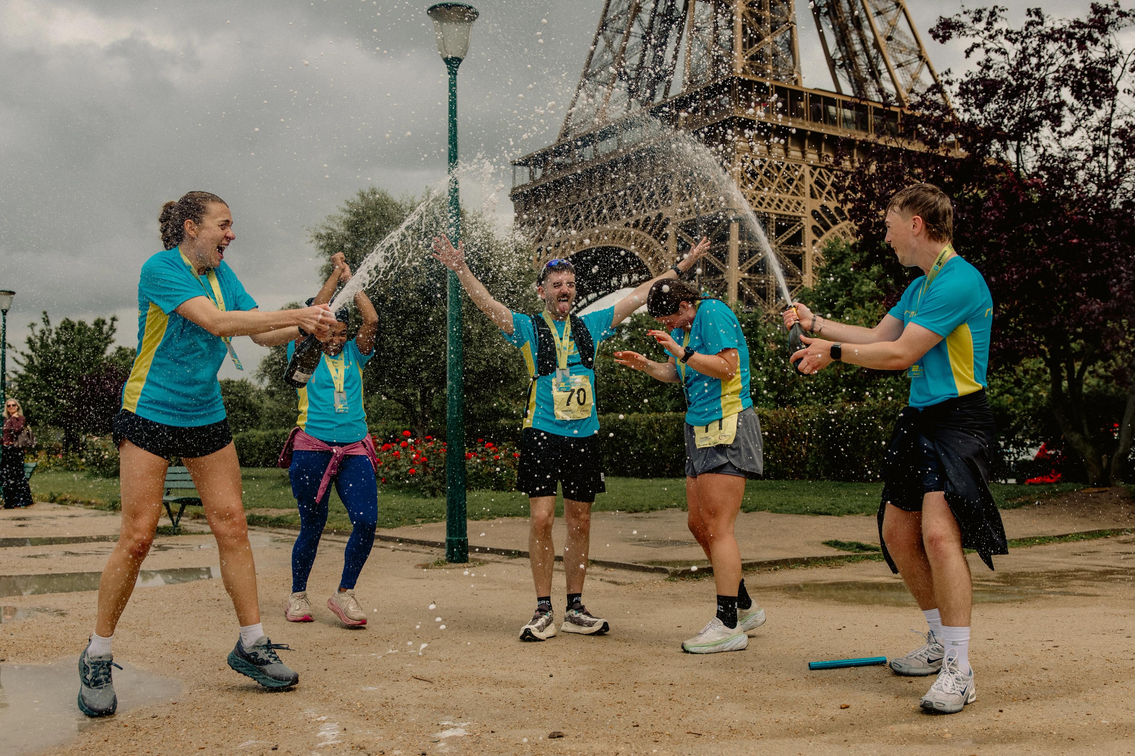 A group of joyful runners sprays champagne on each other near the Eiffel Tower.