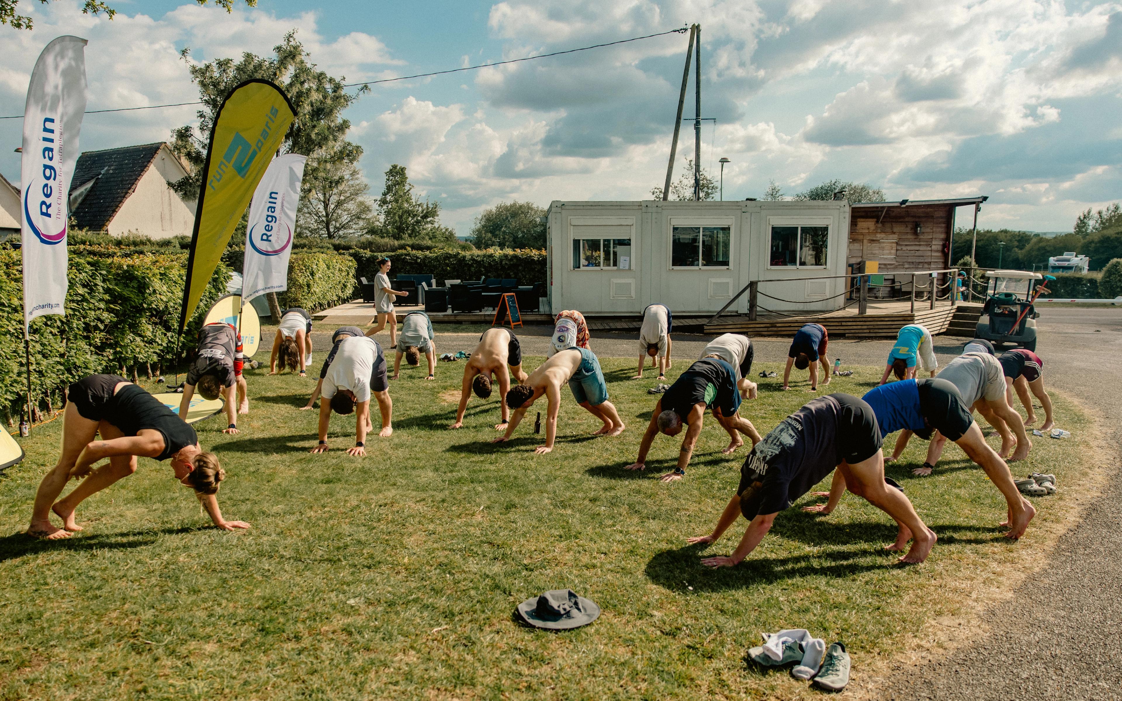 A group of people performing yoga in a downward dog pose on a green lawn.