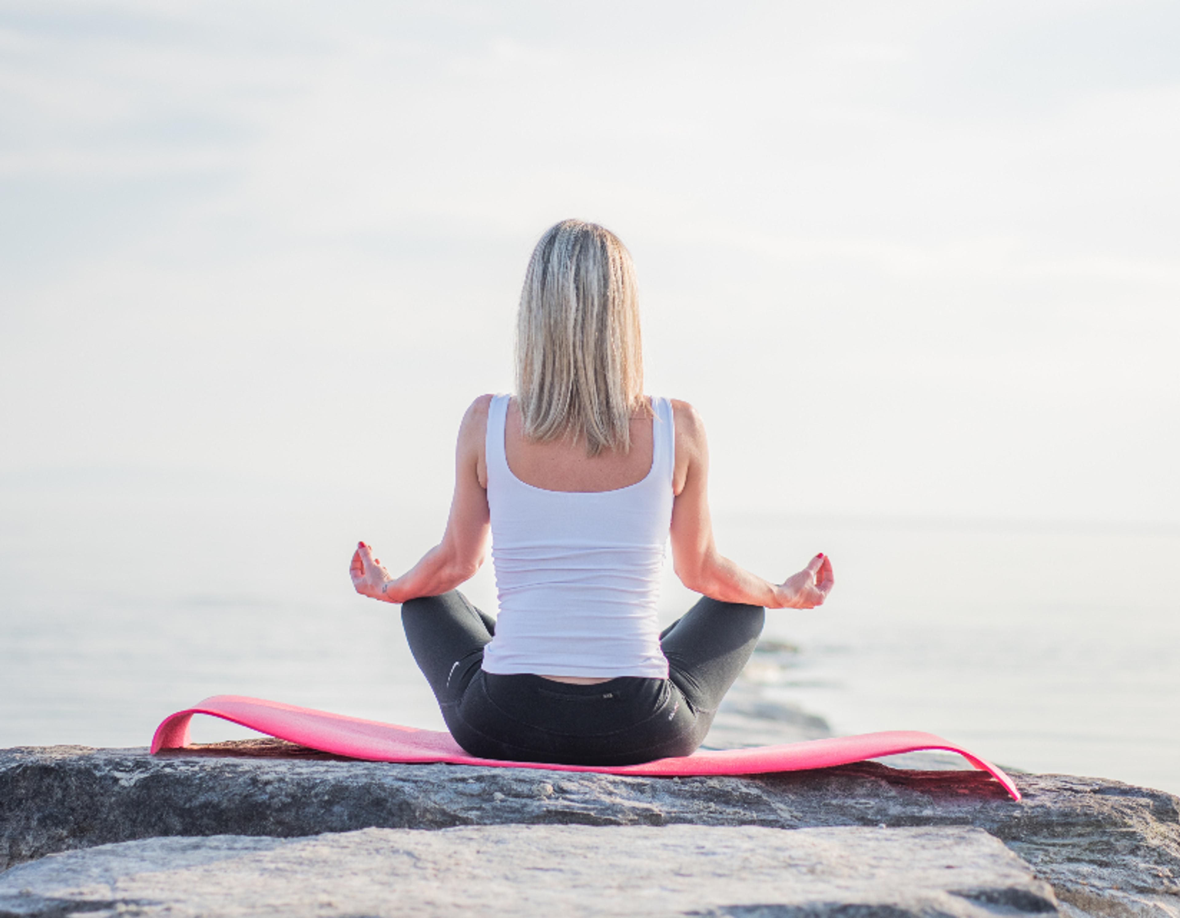 A person meditating outdoors at sunrise.