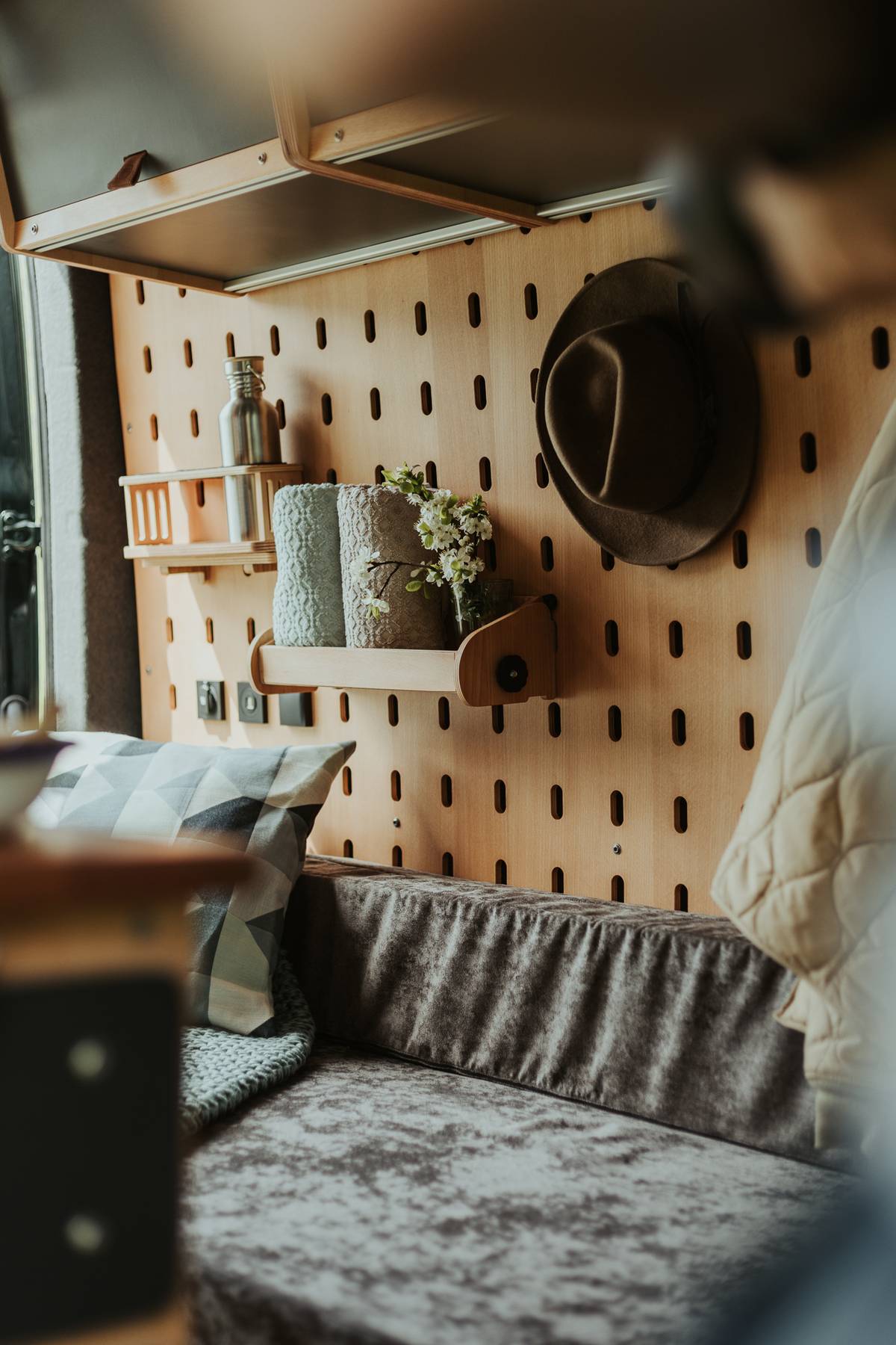 Interior of a converted camper van with a wooden pegboard, a hat and a bench