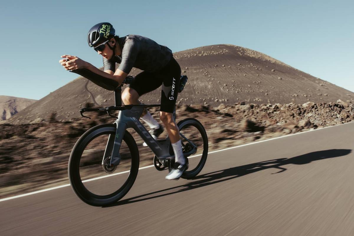 Cyclist in aero position on a time-trial bike passing a volcanic cone