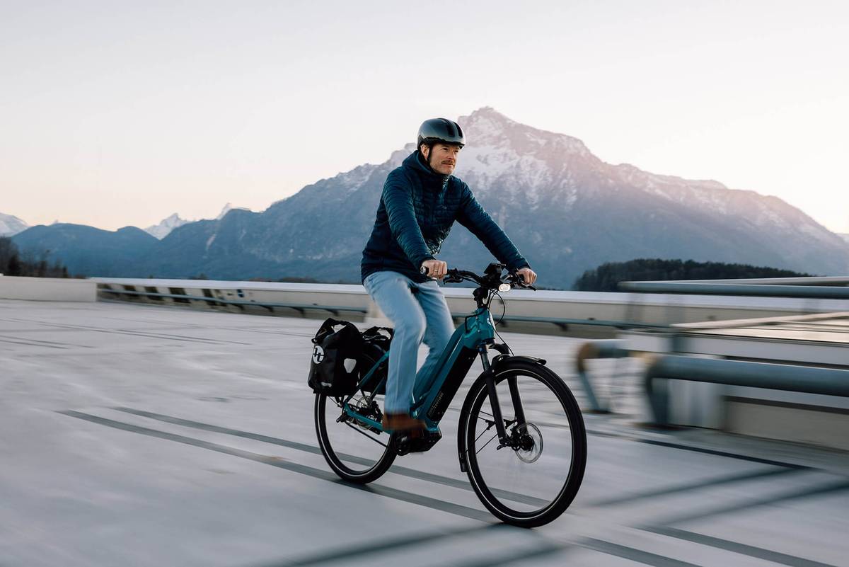 Radfahrer auf einem E-Bike mit Packtasche, dahinter ein Berg im Abendlicht