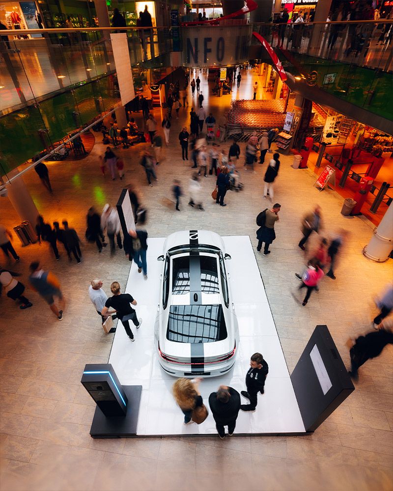 View from above into a shopping centre: visitors around a white car on a display stand
