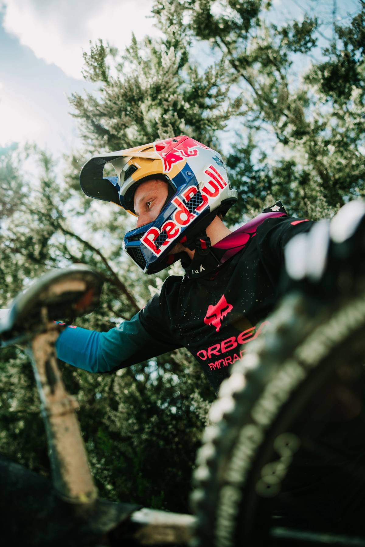 Close-up of a helmeted mountain biker gripping the handlebars on a wooded trail during a production shoot.