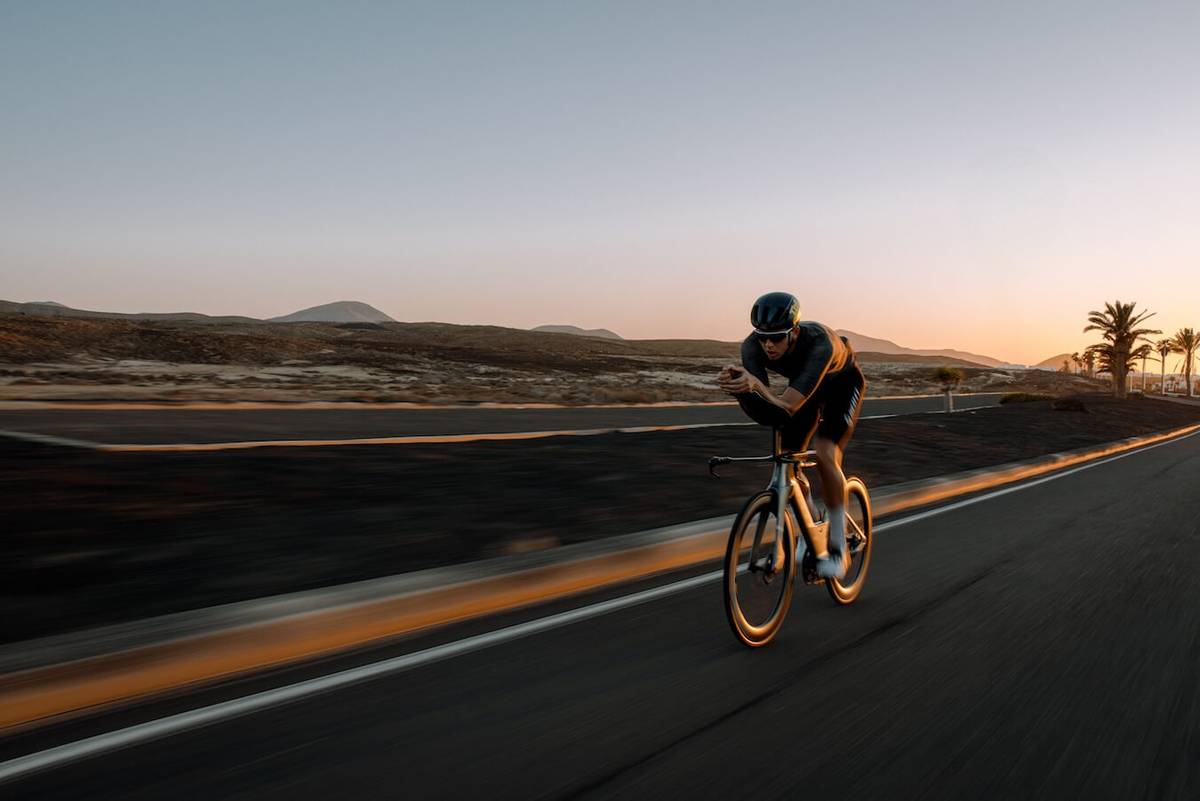 Cyclist on a time-trial bike at dusk, the roadside blurred by speed