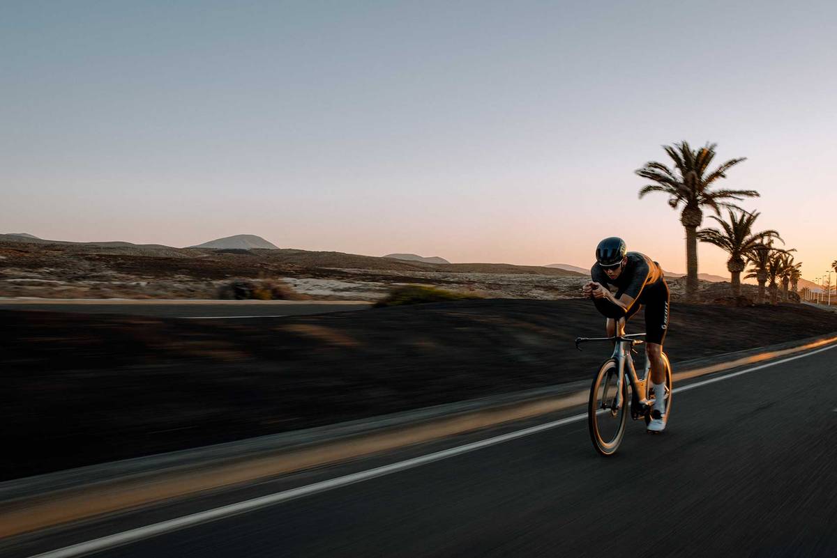 Triathlet auf dem Zeitfahrrad auf einer Straße auf Lanzarote in der Dämmerung, dahinter Palmen