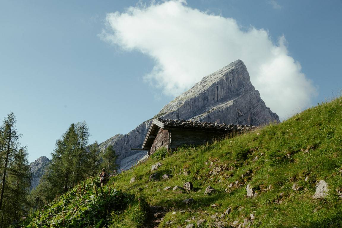 Alte Almhütte auf einem grünen Hang unter einem steilen Felsgipfel