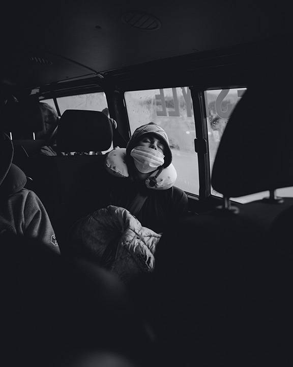 Schwarz-Weiß-Foto: Athlet schläft mit Maske auf der Rückbank eines Teambusses
