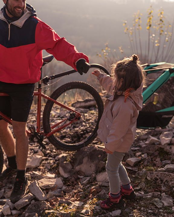 A man holds his mountain bike while a small child touches the front wheel