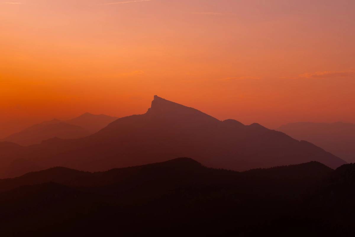 The Schafberg ridge in silhouette against an orange-red evening sky, a striking peak in the middle