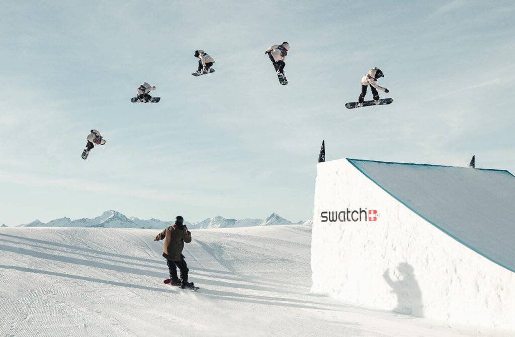 Sequenzaufnahme eines Snowboarders im Sprung über einen großen Kicker, ein Fahrer schaut zu