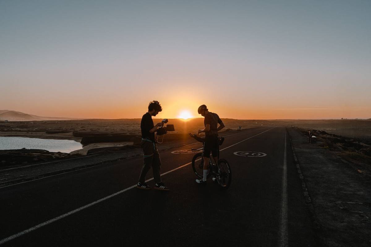 Silhouettes of a camera operator and the cyclist on a road at sunset