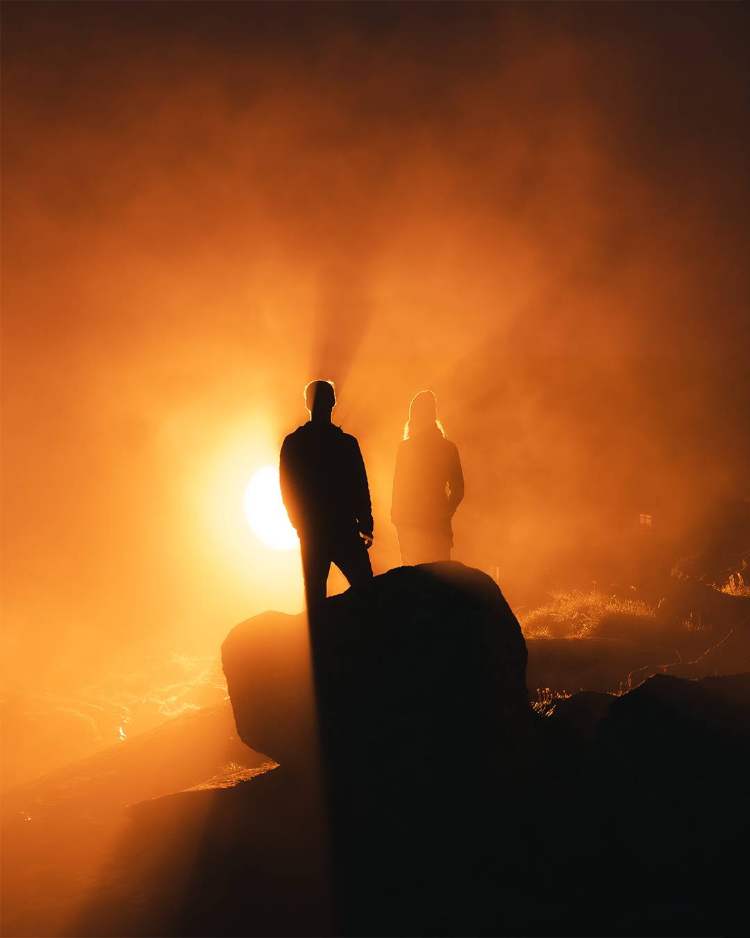 Two silhouettes on a rock, backlit in orange haze