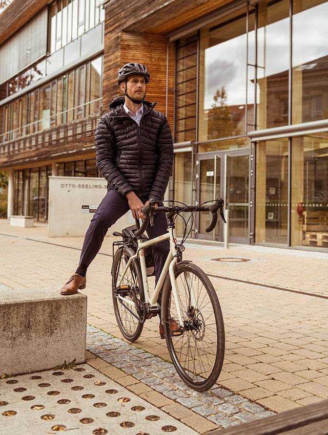 Man in a helmet and down jacket on a light-coloured bike in front of a wooden building