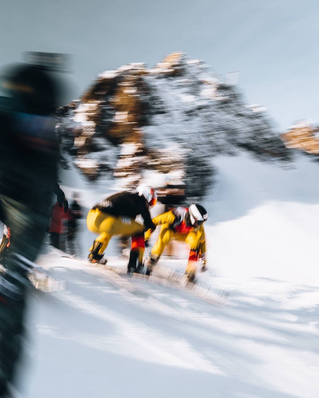 Motion-blurred shot of a group in yellow trousers in the snow below a rocky peak