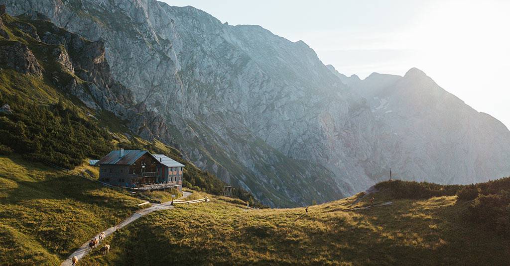 Mountain hut on an alpine meadow below steep rock faces in the evening light