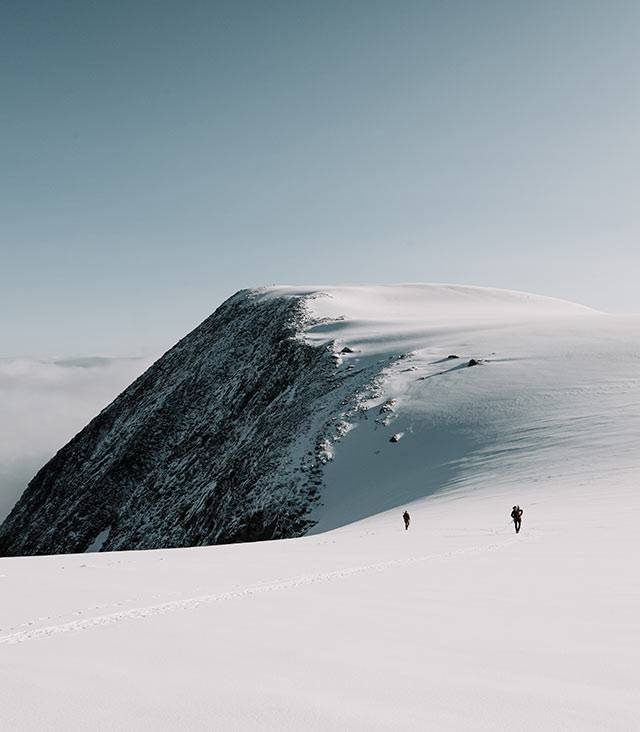 Two mountaineers crossing a wide snowfield below a rocky ridge