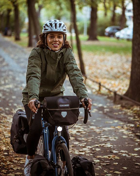 Smiling woman with a helmet riding a touring bike with panniers along an autumn avenue