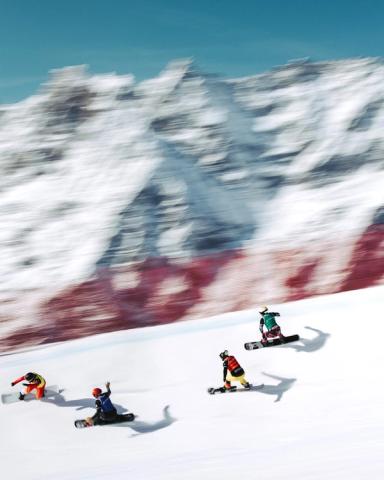 Mitzieher: vier Snowboardcrosser im Rennen, der Berg im Hintergrund verwischt