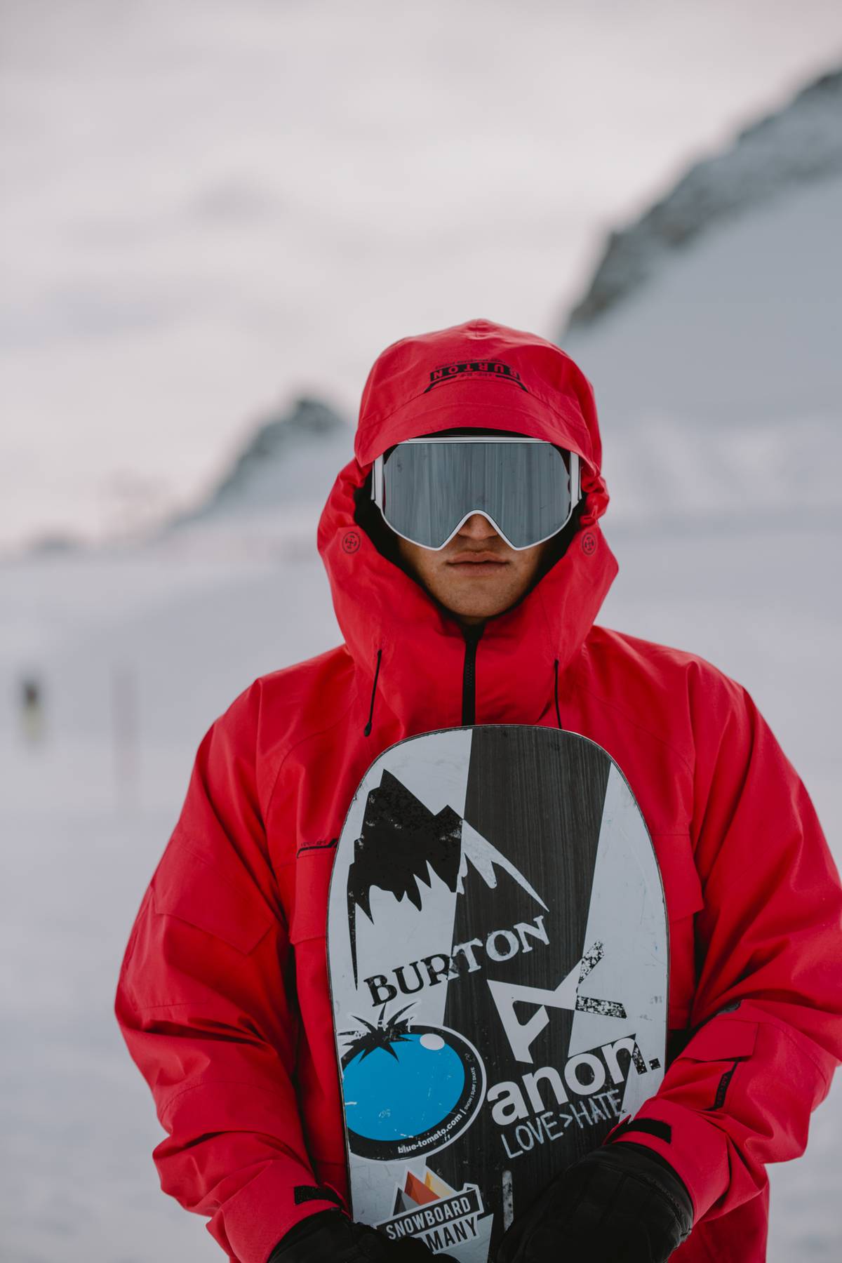 Snowboarder in a red jacket and goggles holding the board in front of the chest