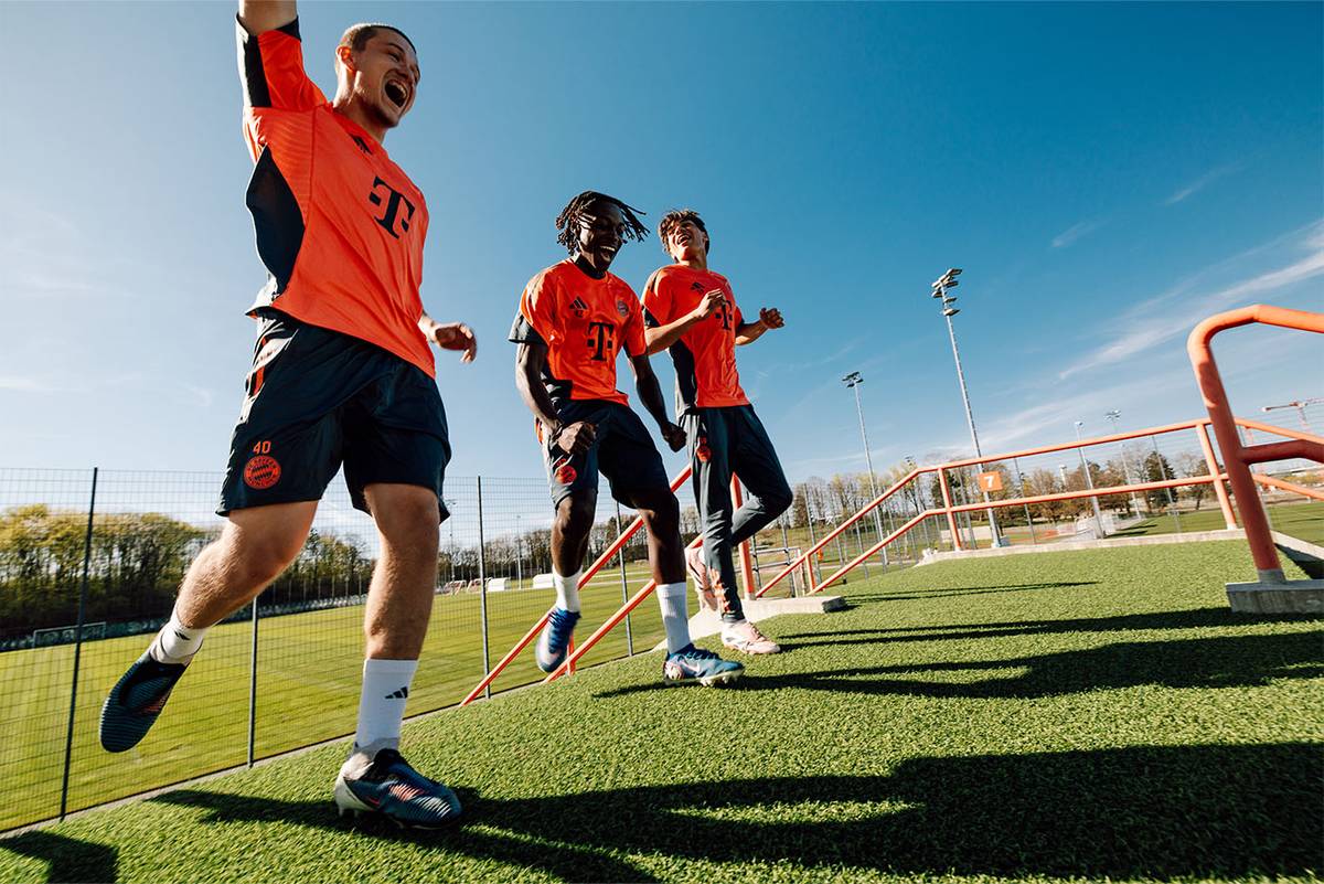 Drei Spieler lachen und springen auf dem Trainingsplatz unter blauem Himmel