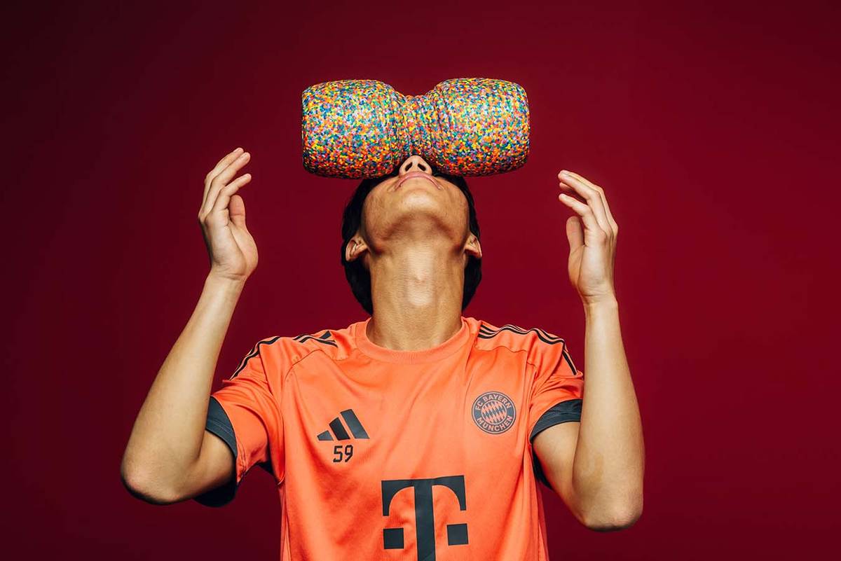 Spieler balanciert eine bunte Faszienrolle auf der Stirn, roter Hintergrund
