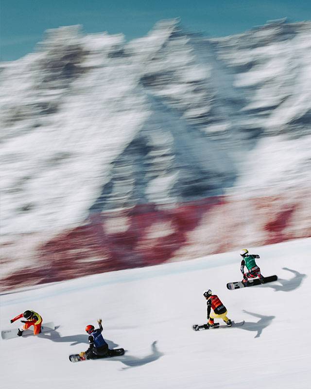 Vier Snowboardcross-Fahrer im Rennen auf der Strecke, Hintergrund in Bewegungsunschärfe
