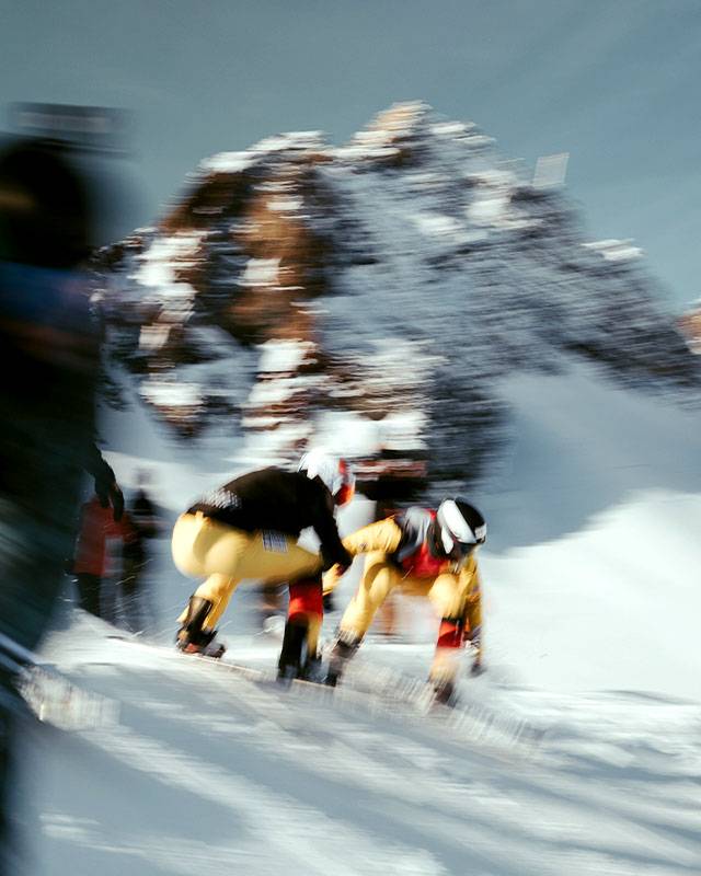 Zwei Snowboardcross-Fahrer in gelben Rennanzügen Seite an Seite, mit Bewegungsunschärfe