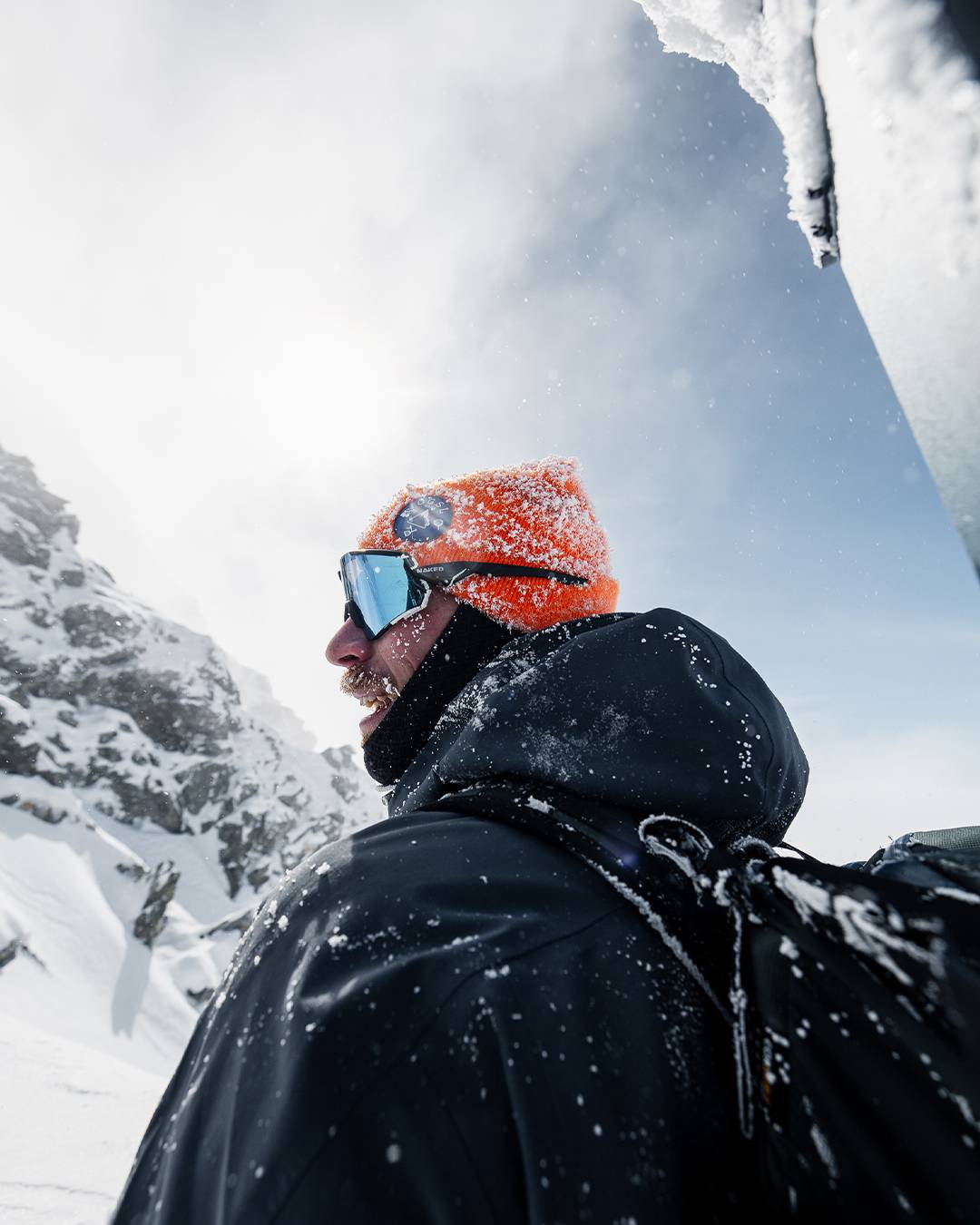 Person in an orange beanie, goggles and a backpack in driving snow, photographed from below