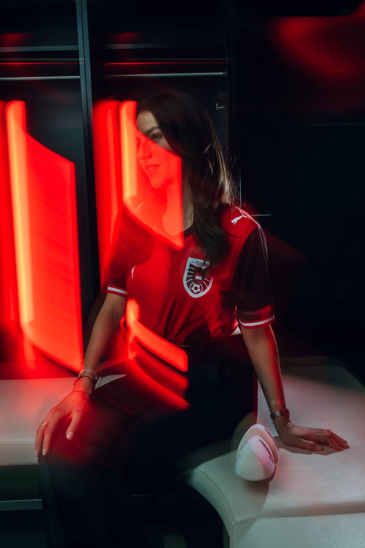 A woman in a red football jersey poses on a white sofa amid glowing red light panels.