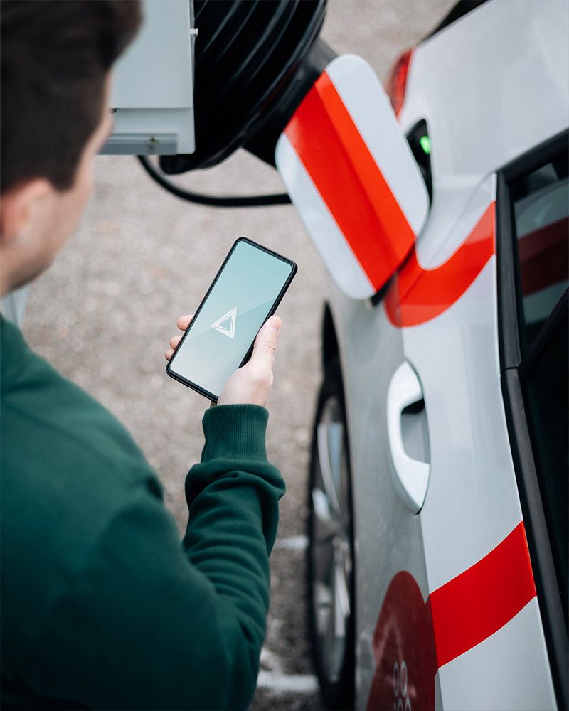 Man holding a phone with the Alveri app next to a car being charged by a charging robot