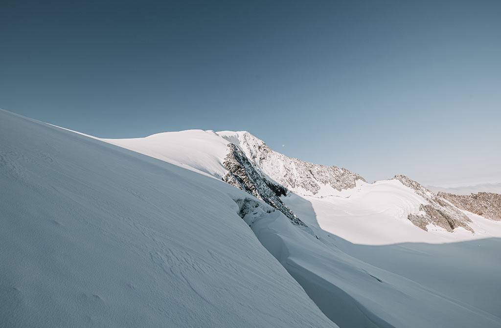 Snow-covered glacier slope below a summit under a clear sky