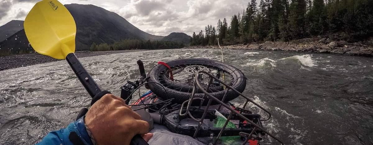 Blick vom Packraft auf einen reißenden Fluss, vorne ein festgezurrtes Fahrrad