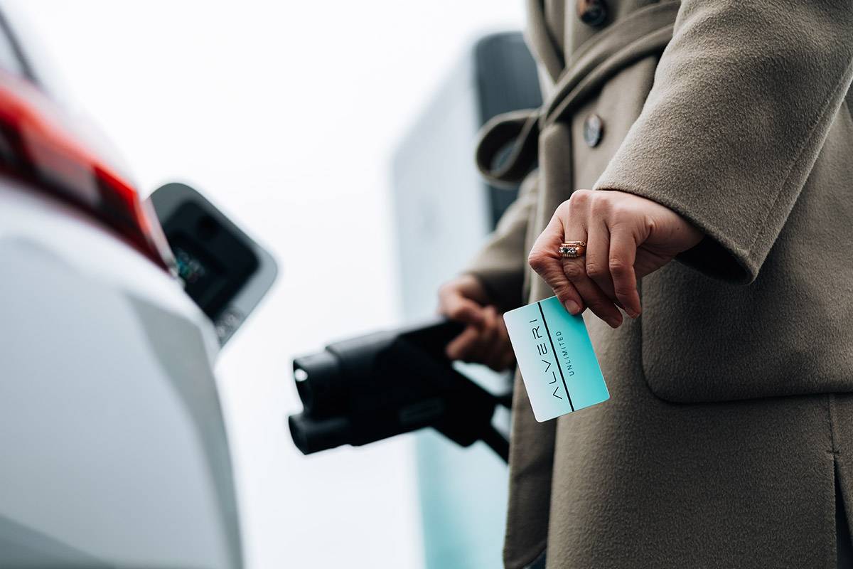 Hand holding an Alveri charging card next to a charging plug