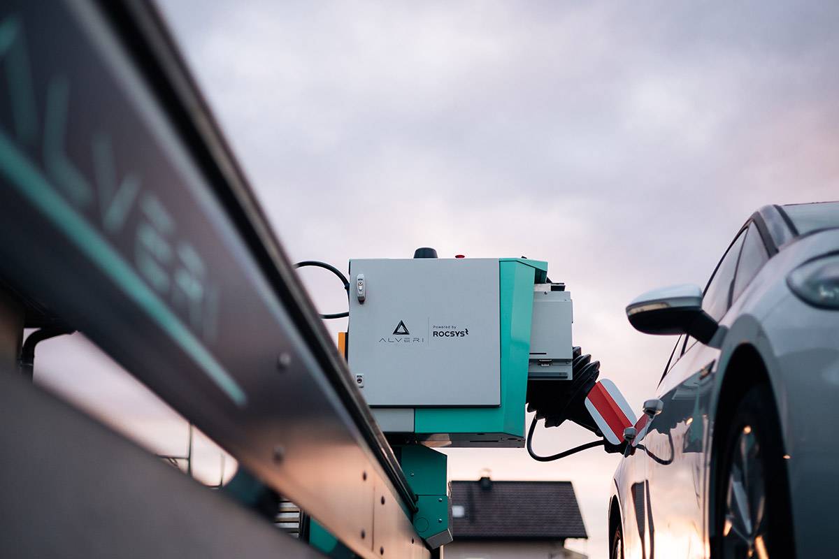 Charging robot on a rail docking onto an electric car under evening clouds