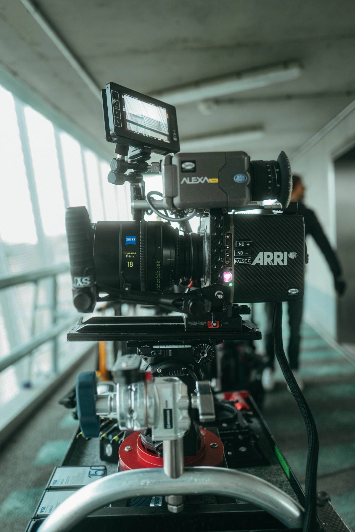 A cinema camera with a large lens and monitor is mounted on a track, with a crew member blurred in the background.