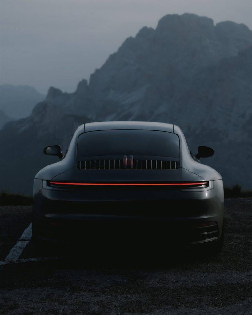 Rear view of a silver sports car with a glowing red taillight against misty mountains.